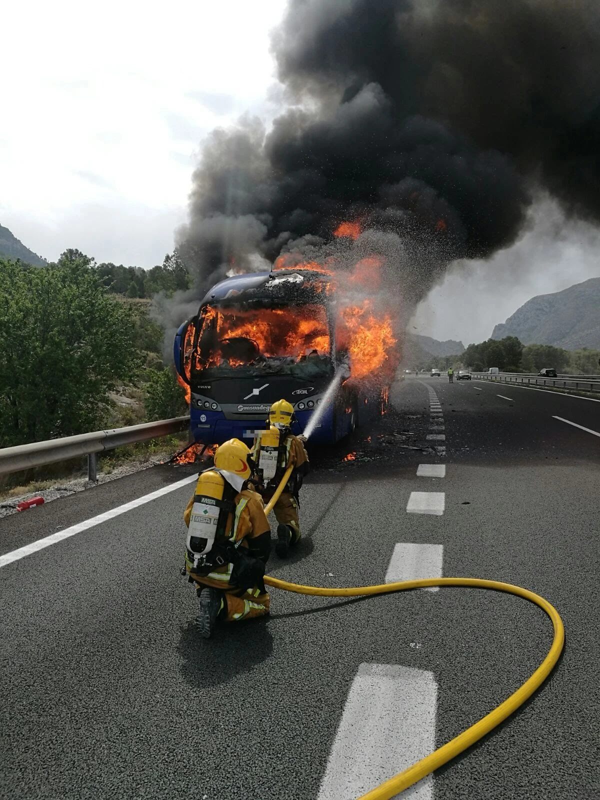 Dos bomberos atacando con agua el incendio de un autobús