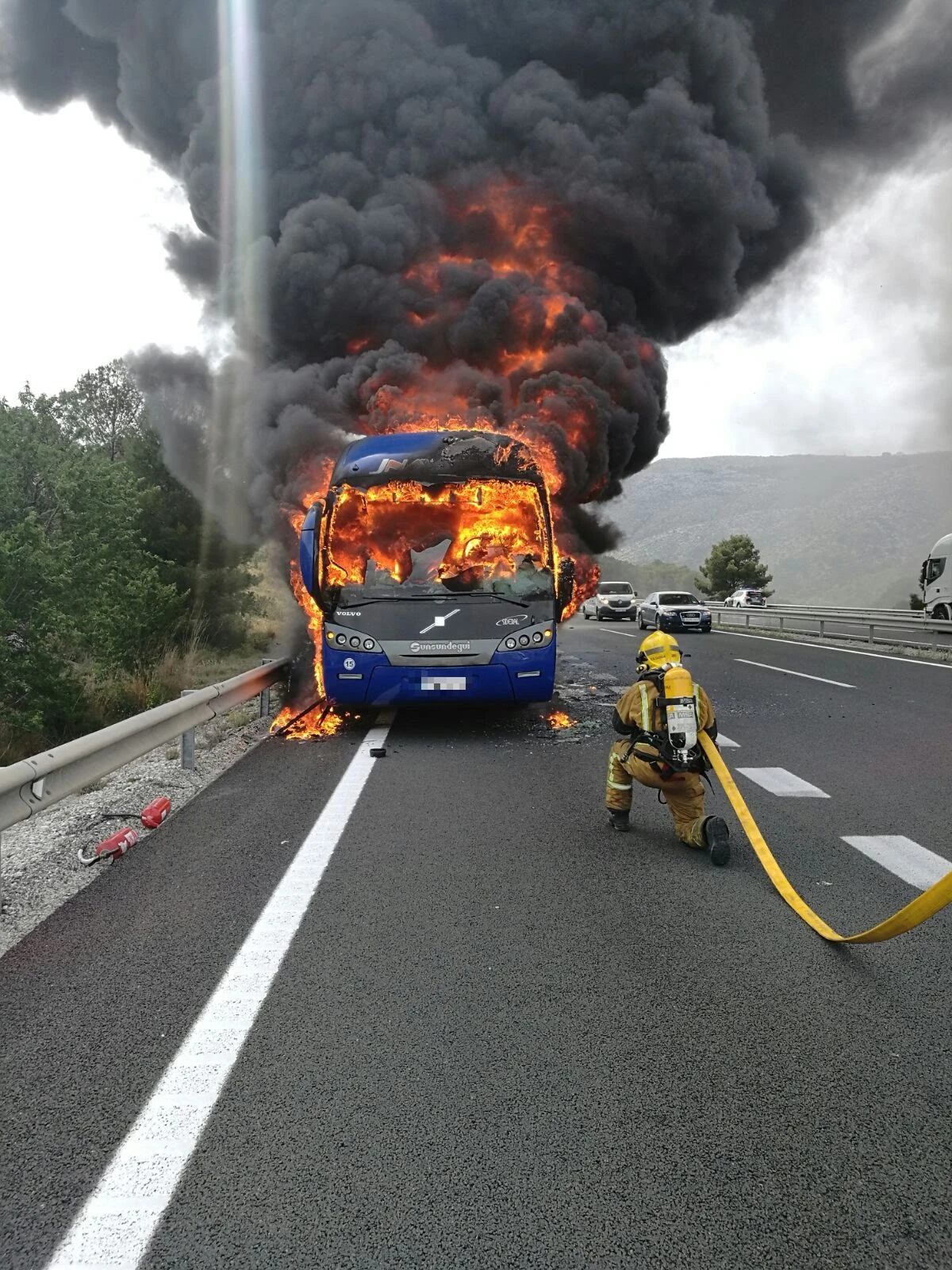 Un bombero preparado frente a un autobús en llamas